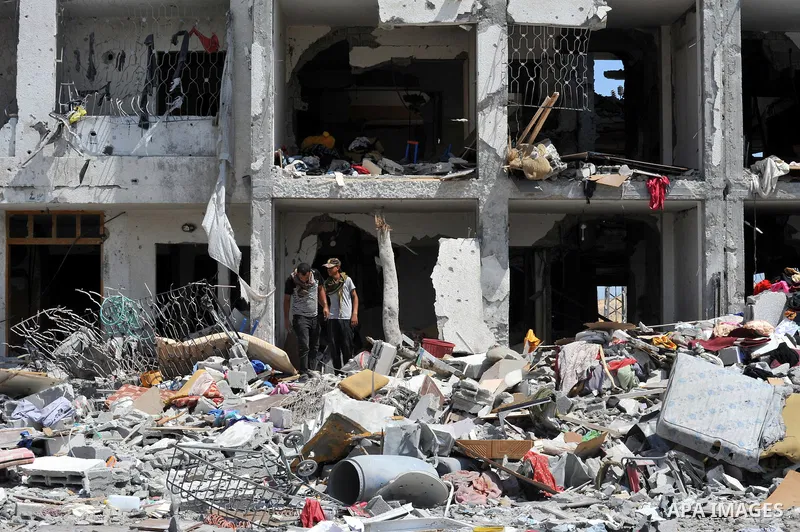 Palestinians walk in front of the rubble of buildings destroyed in Israeli strikes, in Beit Lahiya, northern Gaza Strip, Monday, Aug. 4, 2014.. Photo by Ezz al-Zanoun