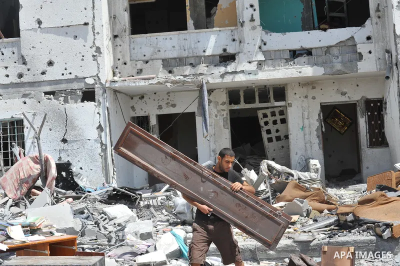 Palestinians walk in front of the rubble of buildings destroyed in Israeli strikes, in Beit Lahiya, northern Gaza Strip, Monday, Aug. 4, 2014.. Photo by Ezz al-Zanoun