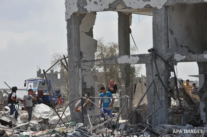 Palestinians walk in front of the rubble of buildings destroyed in Israeli strikes, in Beit Lahiya, northern Gaza Strip, Monday, Aug. 4, 2014.. Photo by Ezz al-Zanoun