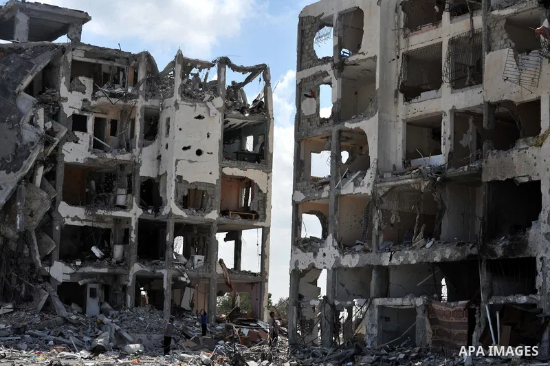 Palestinians walk in front of the rubble of buildings destroyed in Israeli strikes, in Beit Lahiya, northern Gaza Strip, Monday, Aug. 4, 2014.. Photo by Ezz al-Zanoun