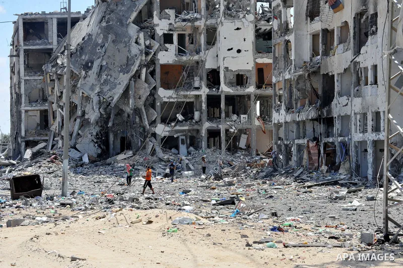 Palestinians walk in front of the rubble of buildings destroyed in Israeli strikes, in Beit Lahiya, northern Gaza Strip, Monday, Aug. 4, 2014.. Photo by Ezz al-Zanoun