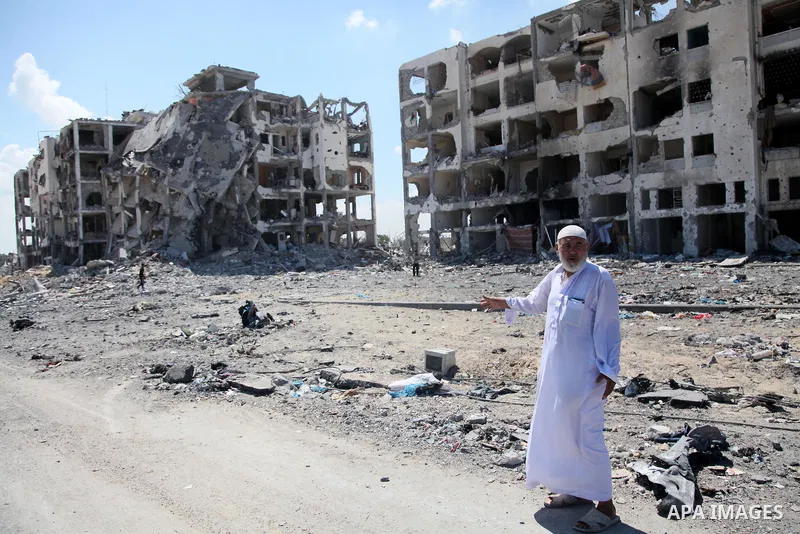 Palestinians walk in front of the rubble of buildings destroyed in Israeli strikes, in Beit Lahiya, northern Gaza Strip, Monday, Aug. 4, 2014.. Photo by Ezz al-Zanoun