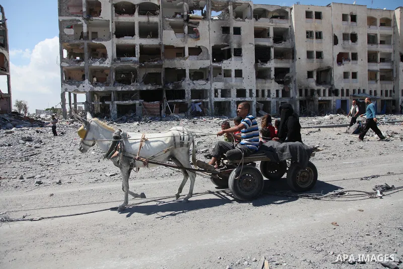 Palestinians walk in front of the rubble of buildings destroyed in Israeli strikes, in Beit Lahiya, northern Gaza Strip, Monday, Aug. 4, 2014.. Photo by Ezz al-Zanoun