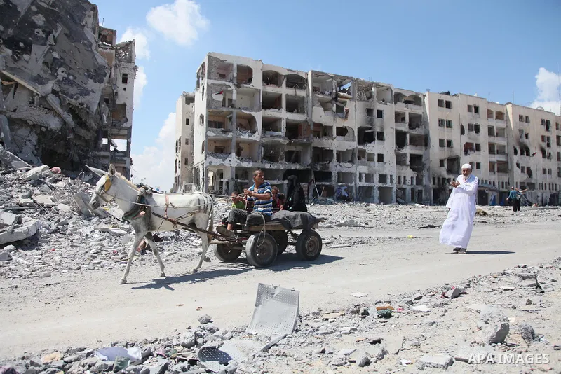 Palestinians walk in front of the rubble of buildings destroyed in Israeli strikes, in Beit Lahiya, northern Gaza Strip, Monday, Aug. 4, 2014.. Photo by Ezz al-Zanoun