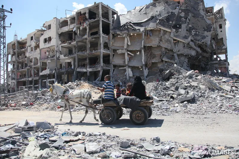 Palestinians walk in front of the rubble of buildings destroyed in Israeli strikes, in Beit Lahiya, northern Gaza Strip, Monday, Aug. 4, 2014.. Photo by Ezz al-Zanoun