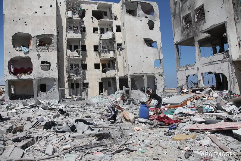 Palestinians walk in front of the rubble of buildings destroyed in Israeli strikes, in Beit Lahiya, northern Gaza Strip, Monday, Aug. 4, 2014.. Photo by Ezz al-Zanoun