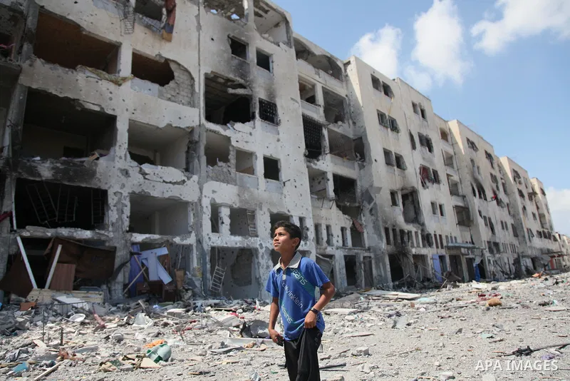 Palestinians walk in front of the rubble of buildings destroyed in Israeli strikes, in Beit Lahiya, northern Gaza Strip, Monday, Aug. 4, 2014.. Photo by Ezz al-Zanoun