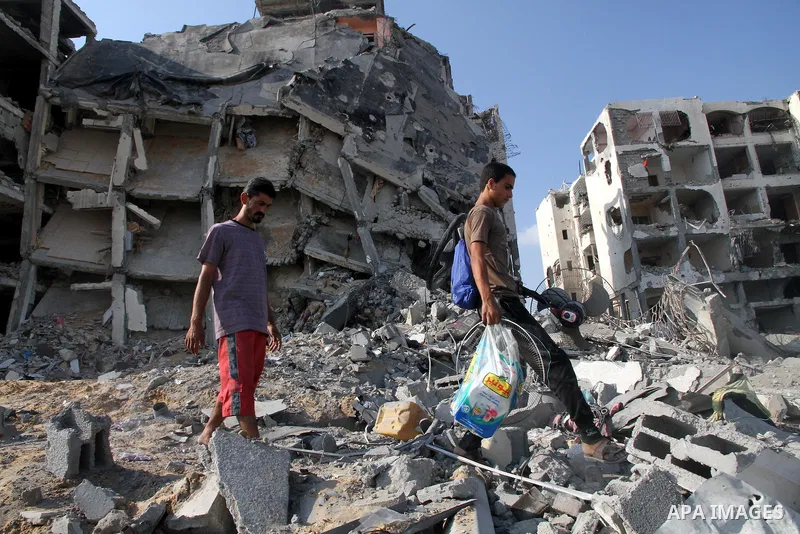 Palestinians carry their belonging as they walk past a badly damaged residential building after returning to Beit Lahiya town, which witnesses said was heavily hit by Israeli shelling and air strikes during the Israeli o...