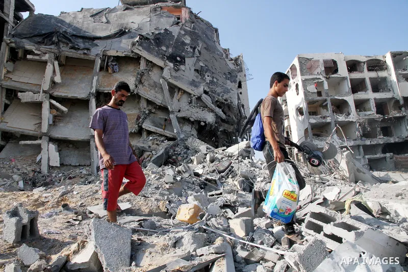 Palestinians carry their belonging as they walk past a badly damaged residential building after returning to Beit Lahiya town, which witnesses said was heavily hit by Israeli shelling and air strikes during the Israeli o...