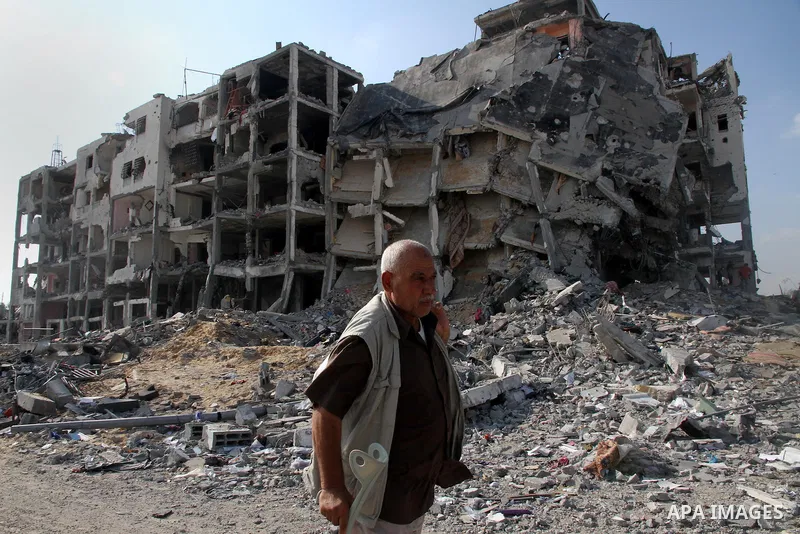 A Palestinian carries his belonging as he walks past a badly damaged residential building after returning to Beit Lahiya town, which witnesses said was heavily hit by Israeli shelling and air strikes during the Israeli o...