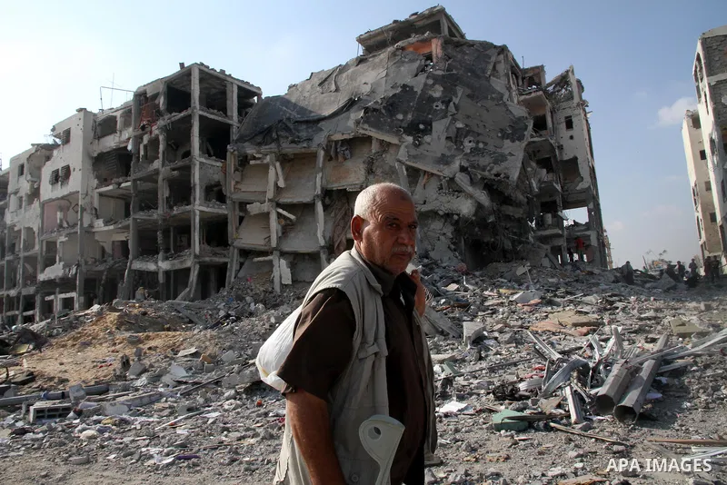 A Palestinian carries his belonging as he walks past a badly damaged residential building after returning to Beit Lahiya town, which witnesses said was heavily hit by Israeli shelling and air strikes during the Israeli o...