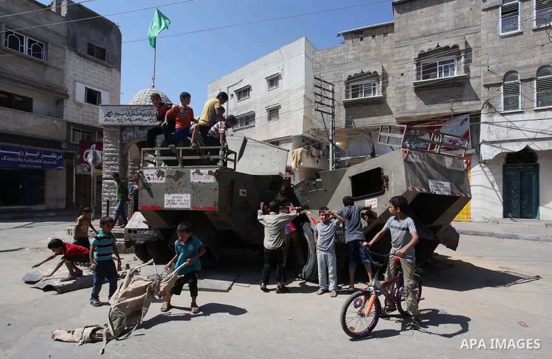 Palestinian children play on the remains of a destroyed Israeli military vehicle, in the east of Khan Younis in the southern Gaza Strip entered a second day, on August 6, 2014. while Israeli and Palestinian delegations p...