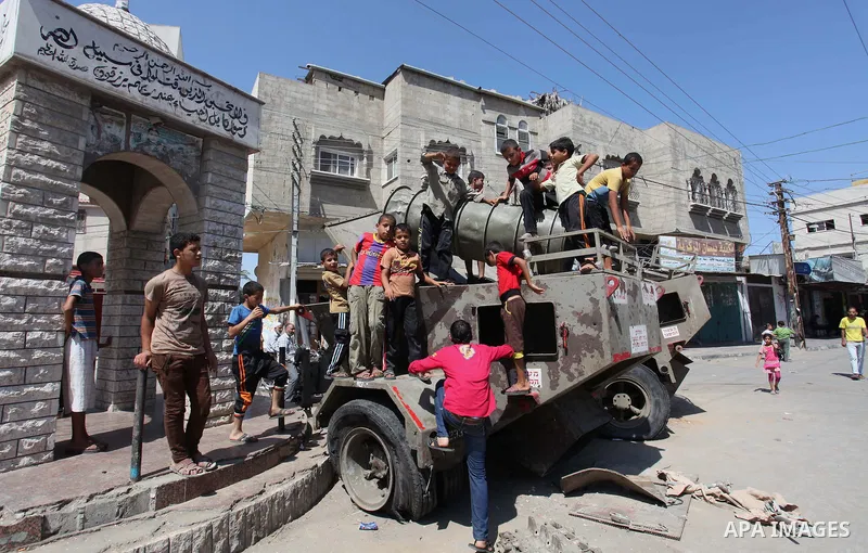 Palestinian children play on the remains of a destroyed Israeli military vehicle, in the east of Khan Younis in the southern Gaza Strip entered a second day, on August 6, 2014. while Israeli and Palestinian delegations p...