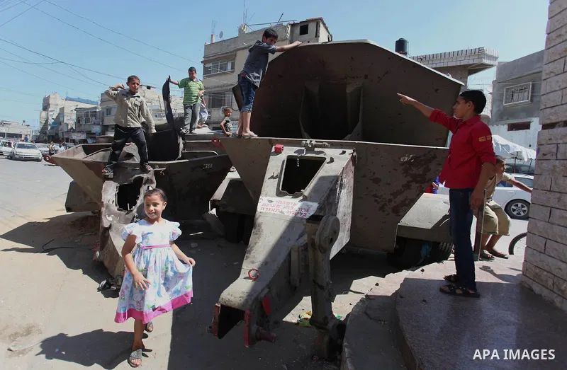 Palestinian children play on the remains of a destroyed Israeli military vehicle, in the east of Khan Younis in the southern Gaza Strip entered a second day, on August 6, 2014. while Israeli and Palestinian delegations p...
