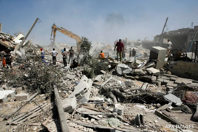 Palestinians watch on as rescuers search for victims under the rubble of a house which was destroyed following an Israeli air strike on Abasan, east of the southern Gaza Strip town of Khan Yunis and close to the border w...