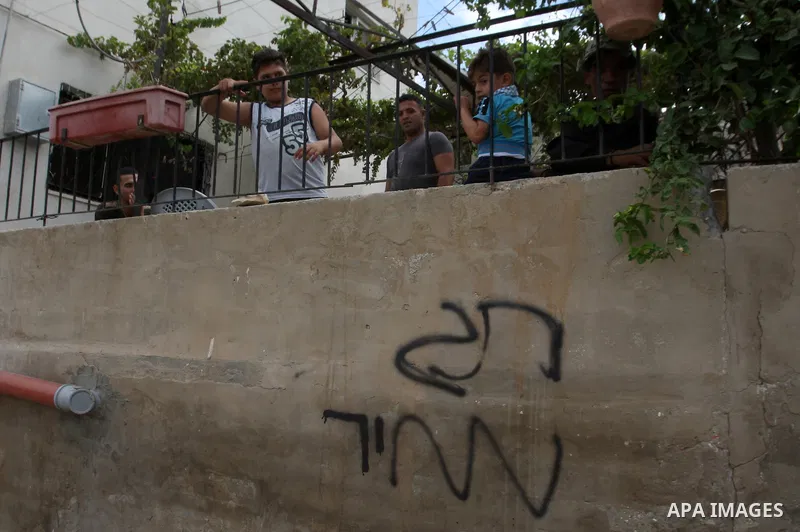 Palestinians stand near a wall of a house which has been painted with graffiti reading in Hebrew "Price Tag" left by Jewish settlers in Yasouf village, near the West Bank city of Salfit, on August 10, 2014. According to...
