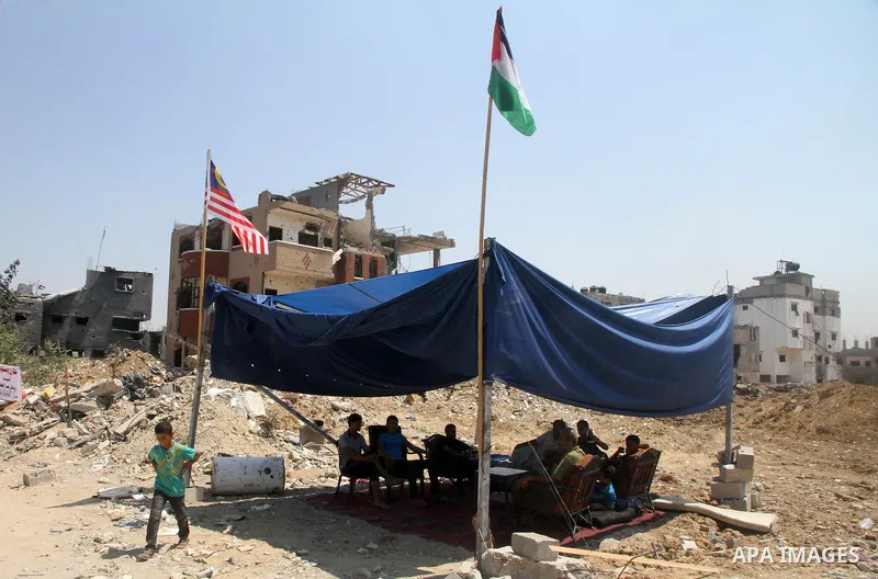 Palestinian and Malaysian flags flutter as Palestinians sit in a tent on the rubble of their house, which witnesses said was destroyed during the Israeli offensive, on the second day of a five-day ceasefire, in the Sheja...