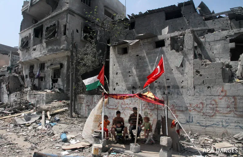 Palestinian and Turkish flags flutter as Palestinians sit in a tent on the rubble of their house, which witnesses said was destroyed during the Israeli offensive, on the second day of a five-day ceasefire, in the Shejaiy...