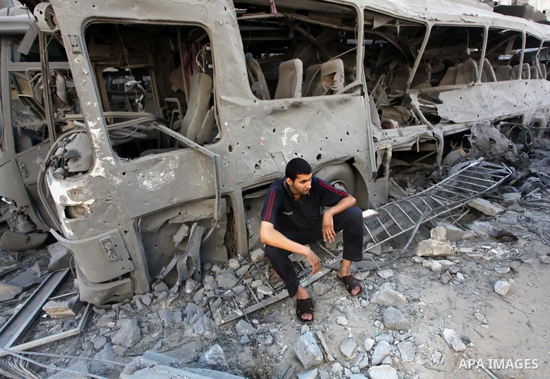 A Palestinian man stands in front of a bus that witnesses said was destroyed during an Israeli airstrike in Gaza City August 20, 2014. Hamas militants in the Gaza Strip fired rockets at Israel for a second day on Wednesd...