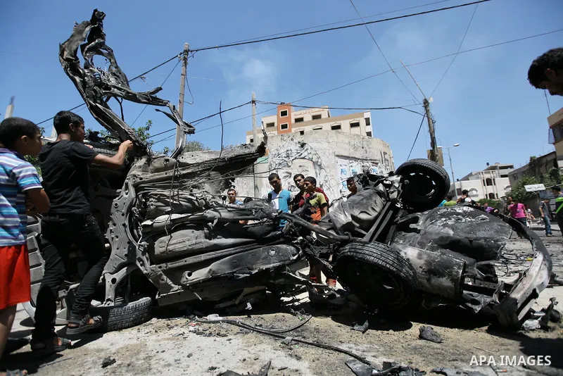 Palestinian gather, in front of a graffiti of late Palestinian leader Yasser Arafat, to inspect a vehicle destroyed following an Israeli military attack in Gaza City on August 21, 2014. The death toll in Gaza rose to 2,0...