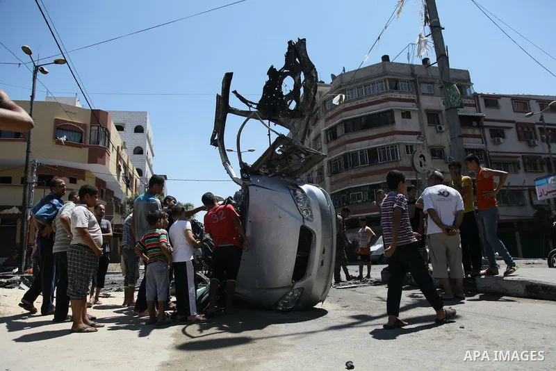 Palestinian gather, in front of a graffiti of late Palestinian leader Yasser Arafat, to inspect a vehicle destroyed following an Israeli military attack in Gaza City on August 21, 2014. The death toll in Gaza rose to 2,0...