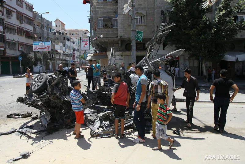 Palestinian gather, in front of a graffiti of late Palestinian leader Yasser Arafat, to inspect a vehicle destroyed following an Israeli military attack in Gaza City on August 21, 2014. The death toll in Gaza rose to 2,0...