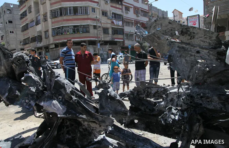 Palestinian gather, in front of a graffiti of late Palestinian leader Yasser Arafat, to inspect a vehicle destroyed following an Israeli military attack in Gaza City on August 21, 2014. The death toll in Gaza rose to 2,0...