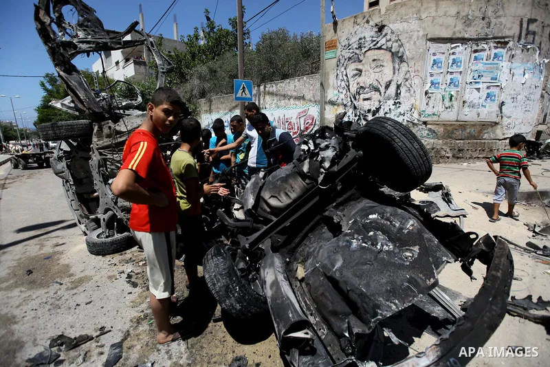 Palestinian gather, in front of a graffiti of late Palestinian leader Yasser Arafat, to inspect a vehicle destroyed following an Israeli military attack in Gaza City on August 21, 2014. The death toll in Gaza rose to 2,0...