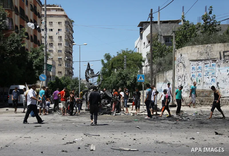Palestinian gather, in front of a graffiti of late Palestinian leader Yasser Arafat, to inspect a vehicle destroyed following an Israeli military attack in Gaza City on August 21, 2014. The death toll in Gaza rose to 2,0...