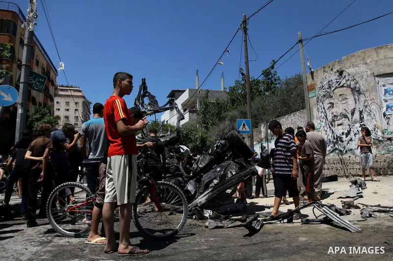 Palestinian gather, in front of a graffiti of late Palestinian leader Yasser Arafat, to inspect a vehicle destroyed following an Israeli military attack in Gaza City on August 21, 2014. The death toll in Gaza rose to 2,0...