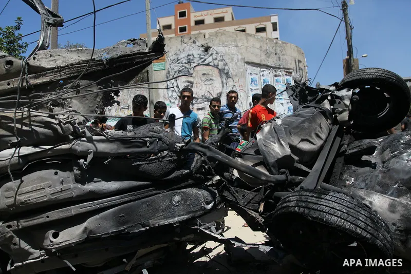Palestinian gather, in front of a graffiti of late Palestinian leader Yasser Arafat, to inspect a vehicle destroyed following an Israeli military attack in Gaza City on August 21, 2014. The death toll in Gaza rose to 2,0...