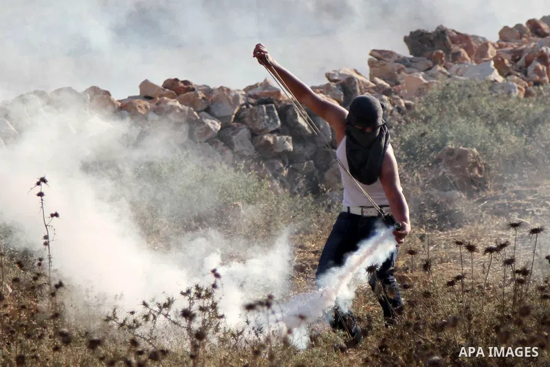 A Palestinian protestors uses a sling shot to throw stones towards Israeli security forces during clashes in the West Bank village of Silwad, near Ramallah, following a demonstration in support of the Hamas militants' re...