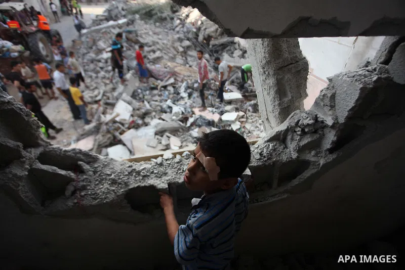 A Palestinian boy standing in his family's damaged house looks up as people inspect the remains of another house, which witnesses said was destroyed by an Israeli air strike, in the central Gaza Strip August 23, 2014. Is...