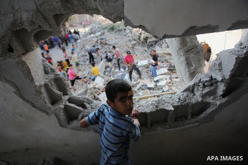 A Palestinian boy standing in his family's damaged house looks up as people inspect the remains of another house, which witnesses said was destroyed by an Israeli air strike, in the central Gaza Strip August 23, 2014. Is...
