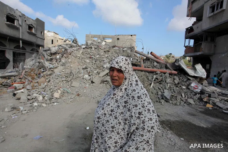 A Palestinian woman looks at the damaged house as the remains of another a house, which witnesses said was destroyed by an Israeli air strike, are seen in the central Gaza Strip August 23, 2014. Israeli aircraft bombed t...