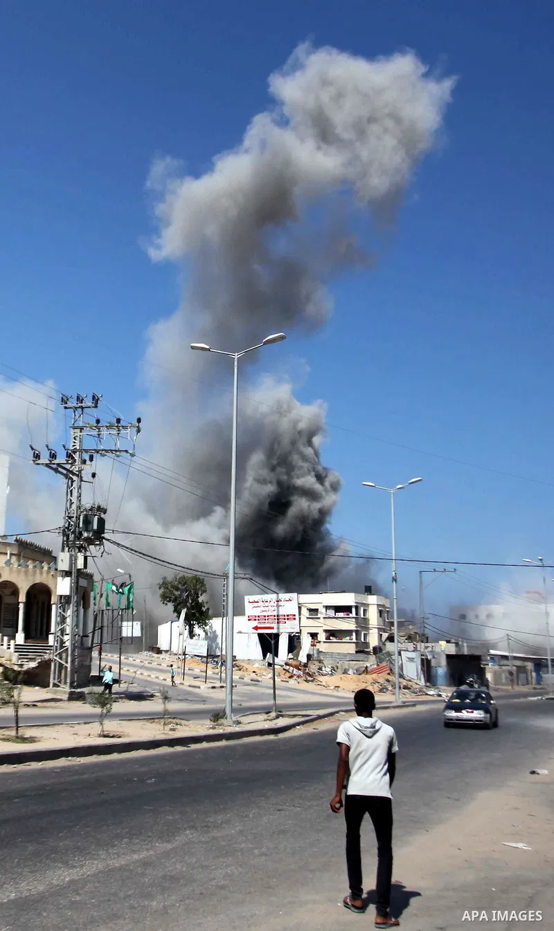 Palestinian men watch as a bomb from an Israeli air strike explodes on target in Gaza City on August 23, 2014. Israeli warplanes pounded Gaza, killing five Palestinians from the same family, two of them children, as the...