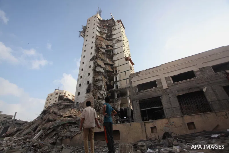 Palestinians stand next to the remains of one of Gaza's tallest apartment towers, which witnesses said was hit by an Israeli air strike that destroyed much of it, in Gaza City August 26, 2014. Israeli air strikes launche...