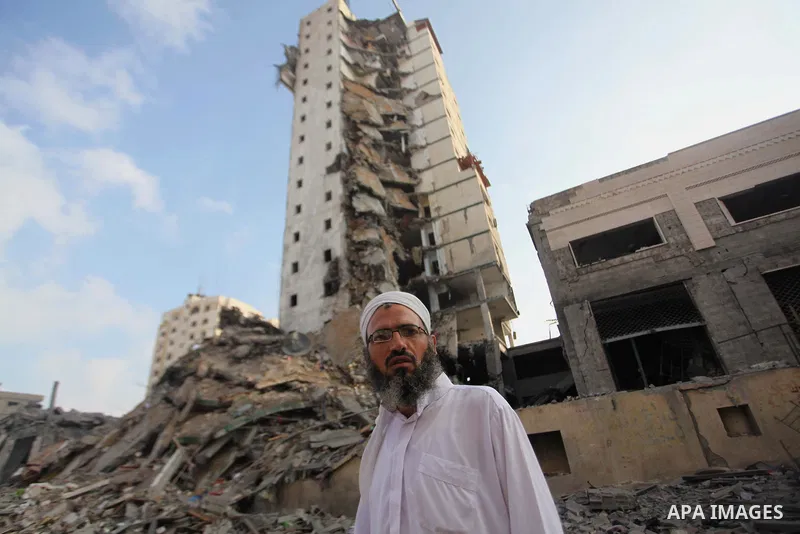 A Palestinian man stands next to the remains of one of Gaza's tallest apartment towers, which witnesses said was hit by an Israeli air strike that destroyed much of it, in Gaza City August 26, 2014. Israeli air strikes l...