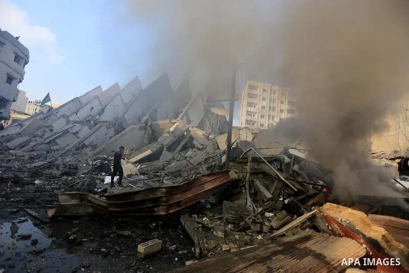 Fire is seen as a Palestinian man walks amidst the remains of a tower building housing offices, which witnesses said was destroyed by an Israeli air strike, in Gaza City August 26, 2014. Israeli air strikes launched befo...