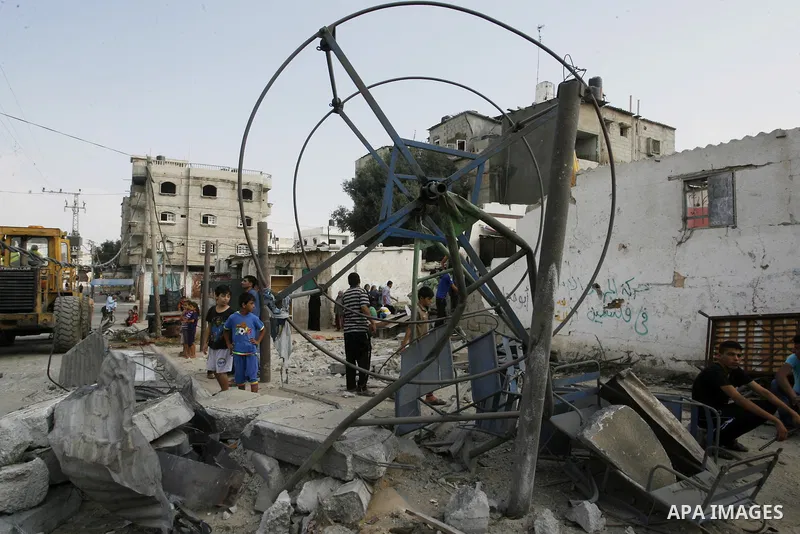 Palestinian children play around a destroyed mini ferris wheel near the remains of homes that were destroyed by an Israeli air strike on Rafah town in the southern Gaza Strip on August 26, 2014. Israeli fire killed 10 Pa...