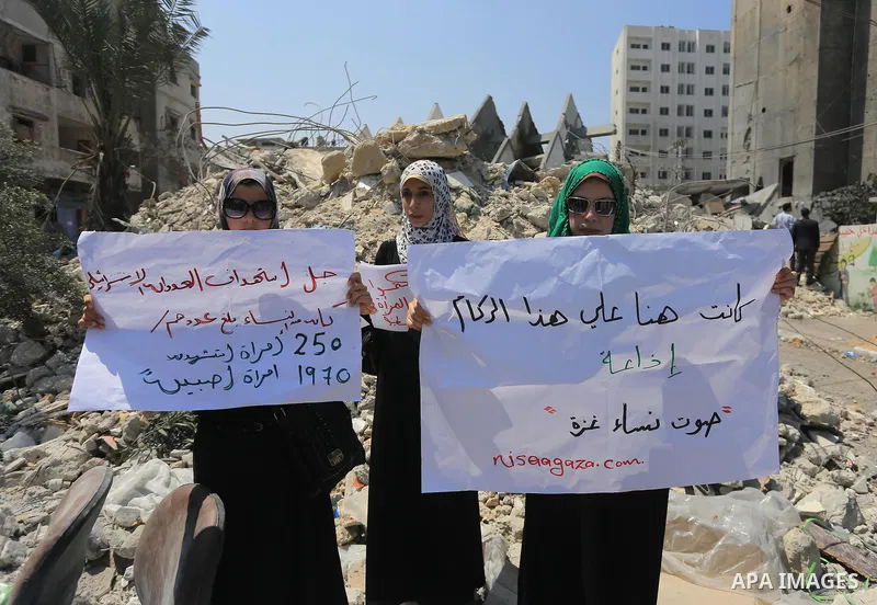Palestinian women hold banners as they take part a protest in front of the El-Basha Tower destroyed by Israeli airstrike in Gaza city on August 28, 2014. Israel and Palestinians both boasted of victory in the Gaza war bu...