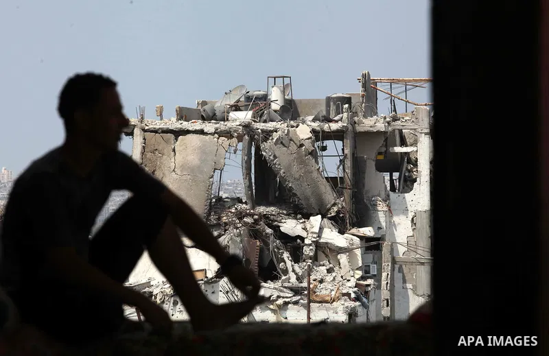 A Palestinian man sits past buildings destroyed during fighting between Hamas militants and Israel in the Al-Shaaf neighbourhood, in Gaza City, on August 31, 2014. An indefinite ceasefire to end seven weeks of fighting b...