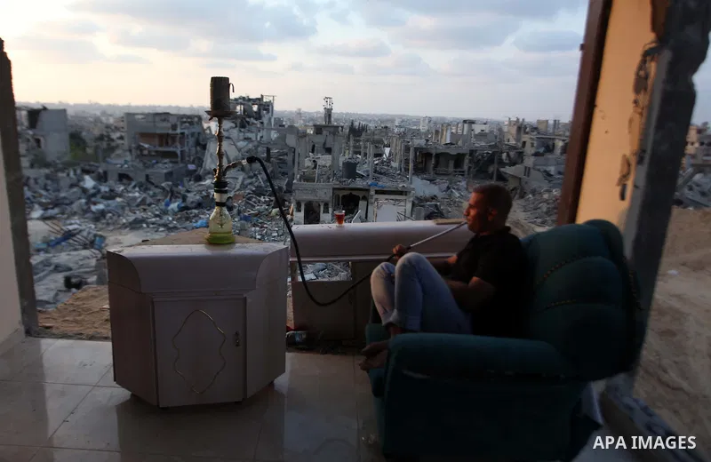 A Palestinian man smokes flavoured tobacco water pipes or 'shisha' inside his destroyed house after returning home in the Tufah neighbourhood in eastern Gaza City on August 31, 2014. Calm returned to the coastal enclave...