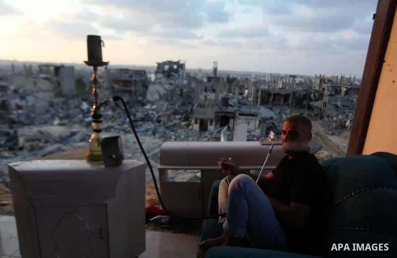 A Palestinian man smokes flavoured tobacco water pipes or 'shisha' inside his destroyed house after returning home in the Tufah neighbourhood in eastern Gaza City on August 31, 2014. Calm returned to the coastal enclave...
