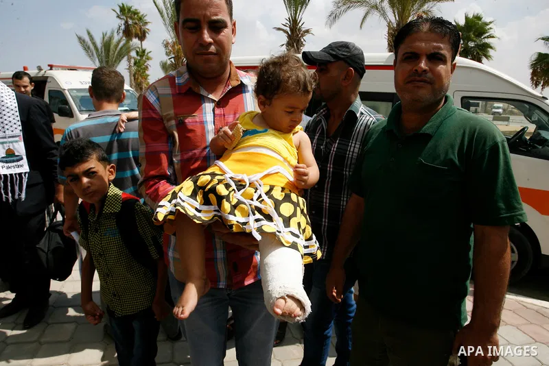 A Palestinian man carries his child, who medics said was wounded during the Israeli offensive on Gaza Strip, waits to be given the permission to cross into Egypt at the Rafah border crossing in the southern Gaza Strip, o...