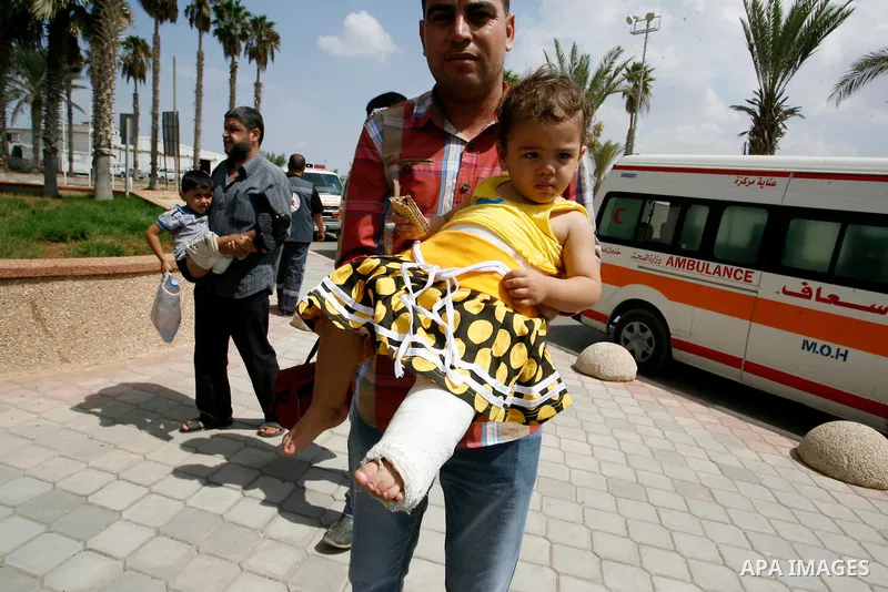 A Palestinian man carries his child, who medics said was wounded during the Israeli offensive on Gaza Strip, waits to be given the permission to cross into Egypt at the Rafah border crossing in the southern Gaza Strip, o...
