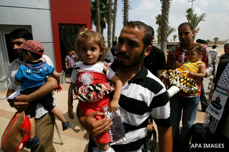 A Palestinian man carries his child, who medics said was wounded during the Israeli offensive on Gaza Strip, waits to be given the permission to cross into Egypt at the Rafah border crossing in the southern Gaza Strip, o...
