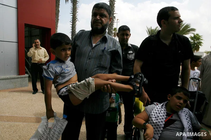 A Palestinian man carries his child, who medics said was wounded during the Israeli offensive on Gaza Strip, waits to be given the permission to cross into Egypt at the Rafah border crossing in the southern Gaza Strip, o...