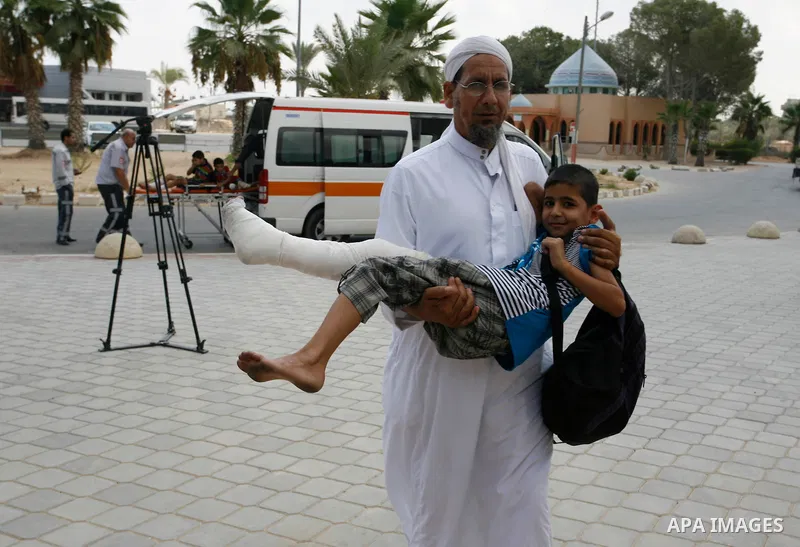 A Palestinian man carries his child, who medics said was wounded during the Israeli offensive on Gaza Strip, waits to be given the permission to cross into Egypt at the Rafah border crossing in the southern Gaza Strip, o...