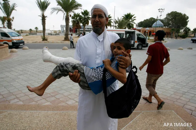 A Palestinian man carries his child, who medics said was wounded during the Israeli offensive on Gaza Strip, waits to be given the permission to cross into Egypt at the Rafah border crossing in the southern Gaza Strip, o...